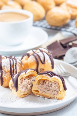 Krem şantili ve çikolatalı ev yapımı profiteroller, erimiş çikolatayla kaplı, kesilmiş, tabakta dikey.