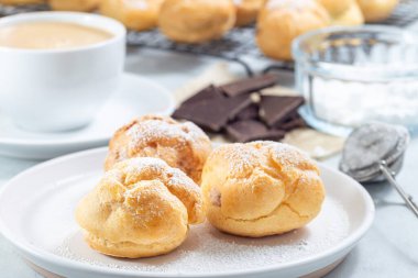 Krem şantili ve çikolatalı ev yapımı profiteroller, kremayla kaplı, tabakta, yatay.