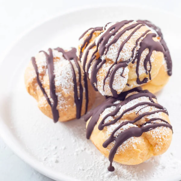 stock image Closeup of profiteroles with whipped cream and chocolate filling, covered with melted chocolate, on a plate, square