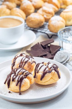 Krem şantili ve çikolatalı ev yapımı profiteroller, erimiş çikolatayla kaplı, tabakta, dikey.
