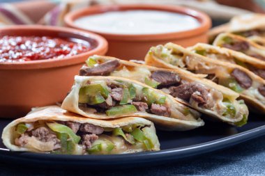 Biftek parçalı Fajita quesadilla, yeşil dolmalık biber, soğan ve peynir, salsa sosu ve ekşi kremayla servis ediliyor, bir tabakta, Meksika mutfağı, yatay yakın plan.