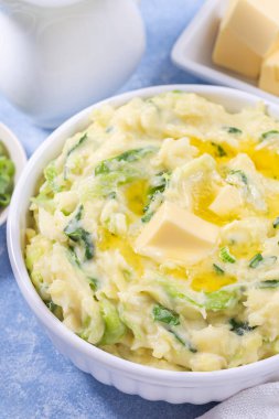 Traditional homemade Irish dish Colcannon or mashed potato with green cabbage and butter, served in white bowl, spring onion and butter on light blue concrete background, St Patrick day food, vertical clipart