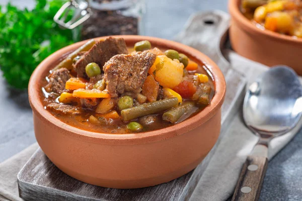 Hearty beef stew with potato, green beans, carrot, celery, peas and corn, in ceramic bowl, horizontal