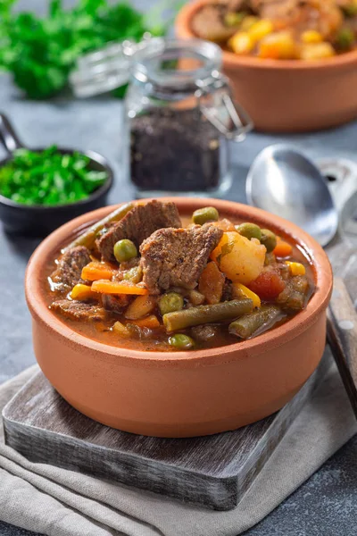 Vegetable beef stew with potato, green beans, carrot, celery, peas and corn, in ceramic bowl, vertical
