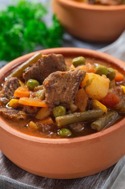 Patatesli biftek güveci, yeşil fasulye, havuç, kereviz, bezelye ve mısır, seramik kasede, dikey, yakın plan.