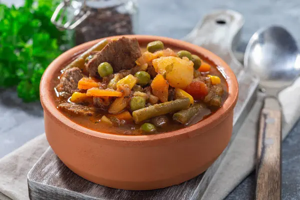 Vegetable beef stew with potato, green beans, carrot, celery, peas and corn, in ceramic bowl, horizontal