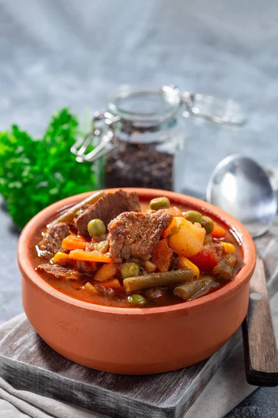 Beef stew with potato, green beans, carrot, celery, peas and corn, in ceramic bowl, vertical, copy space