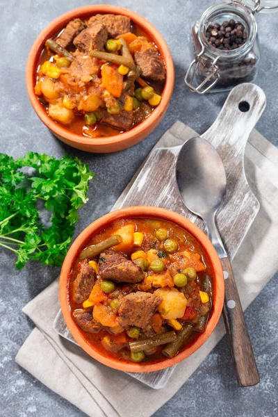 Homemade beef stew with potato, green beans, carrot, celery, peas and corn, in ceramic bowl, vertical, top view