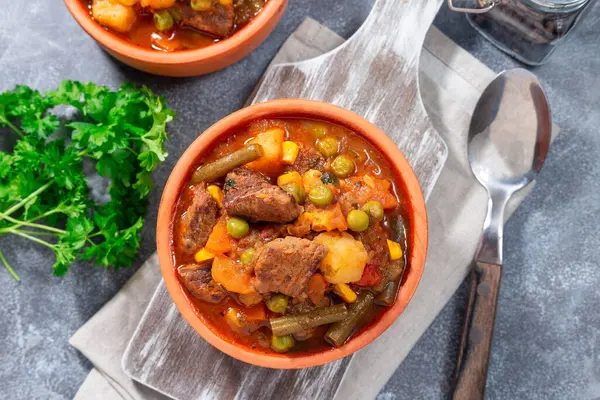 Homemade beef stew with potato, green beans, carrot, celery, peas and corn, in ceramic bowl, horizontal, top view