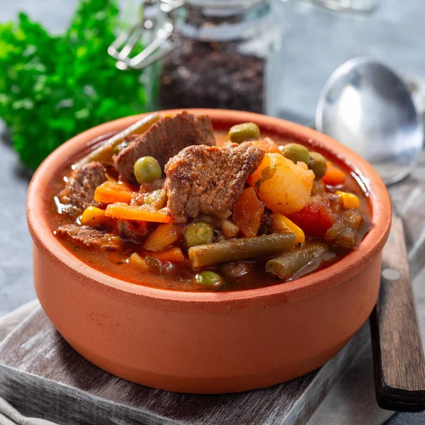 Beef stew with potato, green beans, carrot, celery, peas and corn, in ceramic bowl, square format