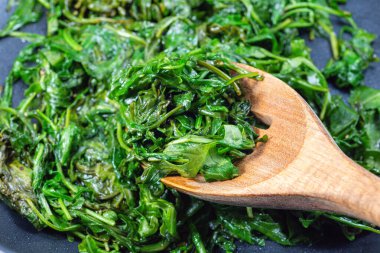 Sarımsak ve balzamik sirkeyle karıştırılmış zeytinyağında pişirilmiş Arugula ya da roket salatası. Kızartma tavasında meze hazırlıyorum, yatay yakın plan.