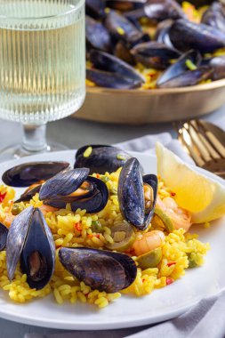 Beyaz bir tabakta, limon ve beyaz şarapla servis edilen midye ve karidesli paella.