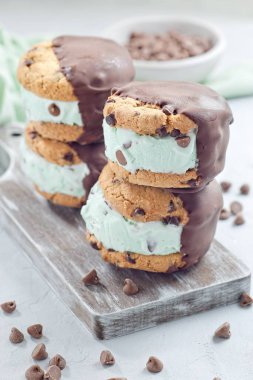 Naneli çikolatalı dondurma ve çikolatalı kurabiye sandviçleri, tahta tahtada, dikey.