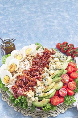 Delicious Cobb salad with greens, tomato, avocado, blue cheese, bacon, rotisserie chicken and boiled eggs, with vinaigrette sauce, on a white plate, vertical copy space