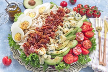 Lezzetli Cobb salatası yeşil, domates, avokado, mavi peynir, pastırma, kızarmış tavuk ve haşlanmış yumurta ile birlikte beyaz bir tabakta, yatay soslu.