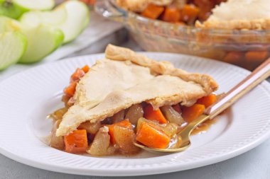 Tatlı patates ve elmalı turta beyaz tabakta altın kaşıklı ve arka planda dilimlenmiş elmalı, yatay yakın plan.