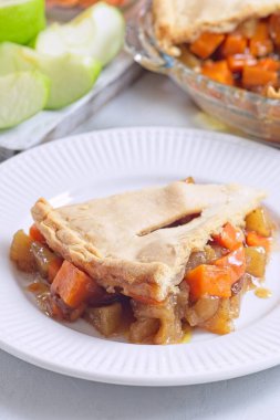 Lezzetli patates ve elmalı turta dilimleri beyaz tabakta, arka planda dilimlenmiş elmalar, dikey.