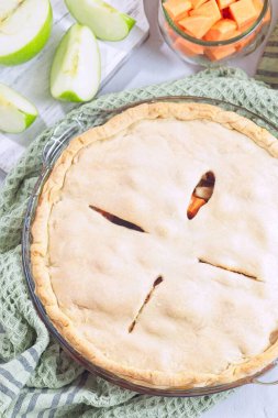 Tatlı patates ve elmalı turta cam tabakta pişiyor, taze elma dilimleri, ve mutfak havlusu sıcacık sonbahar manzarası yaratıyor, dikey, üst manzara