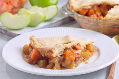 Beyaz tabakta lezzetli patates ve elmalı turta dilimi. Arka planda dilimlenmiş elma, yatay.