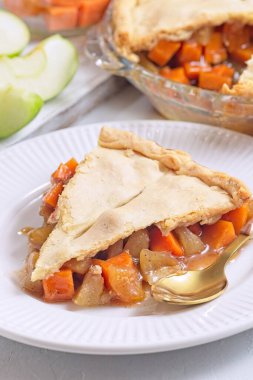 Beyaz tabakta tatlı patates ve elmalı tart, altın kaşıkla, arka planda dilimlenmiş elma, dikey.