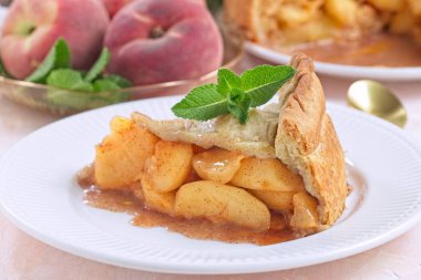 Bir dilim ev yapımı şeftali turtası, taze nane ile süslenmiş, mükemmel bir yaz tatlısı, beyaz tabakta, yatay.