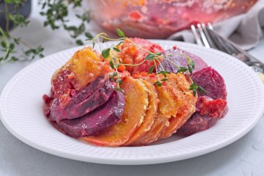 Lezzetli pancar, havuç ve tatlı patates graten, taze kekik ile süslenmiş, beyaz bir tabakta servis edilir, yatay olarak.
