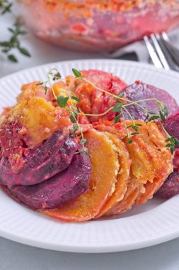 Lezzetli pancar kökü, havuç ve tatlı patates graten, taze kekik ile süslenmiş, beyaz bir tabakta servis edilir, dikey, yakın çekim.