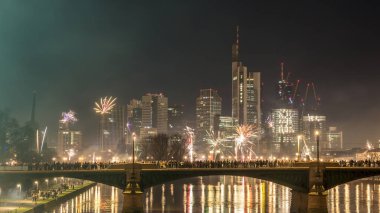 Frankfurt 'un ufuk çizgisi üzerinde havai fişeklerle yeni yıl arifesi soğuk bir kış gecesinde suda renkli yansımalarla.