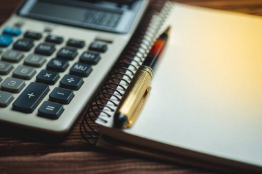 Ahşap bir arka planda makro hesap makinesi, kalem ve defter. İş, finans, eğitim kavramı