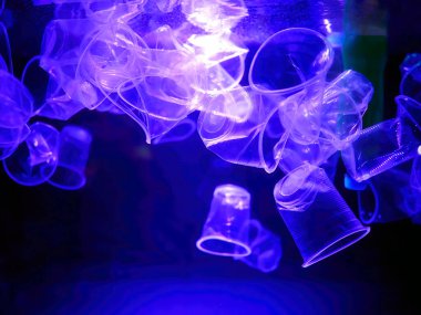 Plastic cups and bottles garbage drifting in an illuminated blue lights water, monochrome, global environment pollution, underwater garbage, Plastic pollution