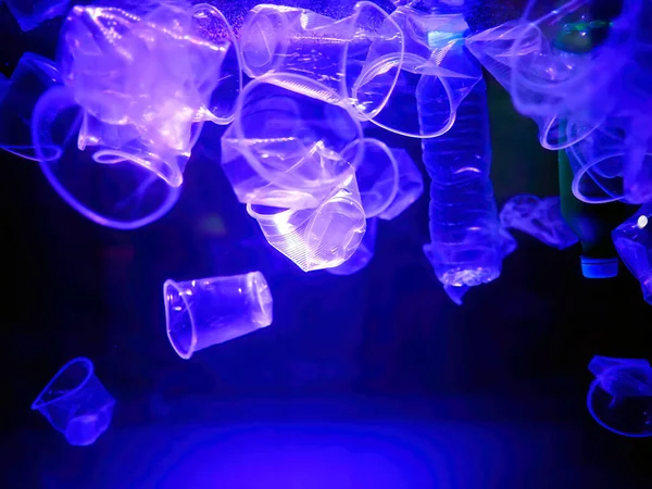 Plastic cups and bottles garbage drifting in an illuminated blue lights water, monochrome, global environment pollution, underwater garbage, Plastic pollution