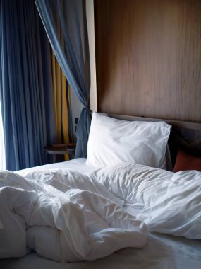Buruşuk beyaz çarşaflar yastıklı ve battaniyeli yumuşak sabah ışıkları, rahat bir yatak odası ve dinlenme havası, yapılmamış boş yatak odası otel işi konsepti, dağınık.