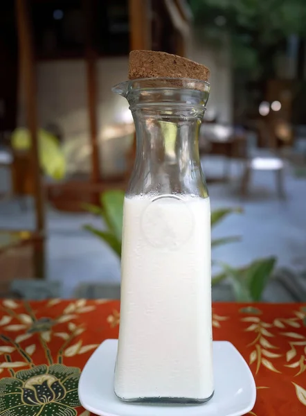 A glass bottle contained plain milk with cork, fresh beverage, utensil, modern product design, bottle design on Thai local pattern table cloth, traditional art fabric, textile