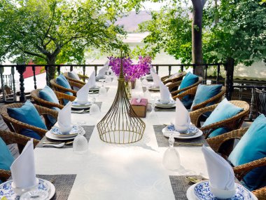 Romantik atmosfer öğle yemeği ya da akşam yemeği için lüks Tayland tarzı sofra takımı, eski seramik çömlek mavi ve beyaz desenli, pirinç nesnelerle süslenmiş beyaz masa örtüsü.