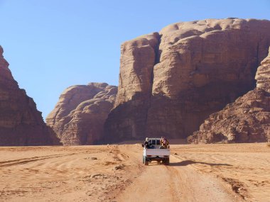 Wadi Rum Çölü 'nde bir kamyonet, kırmızı ve turuncu kum tepecikleri manzarası, UNESCO Dünya Mirası alanı, Açık Hava Ulusal Parkı, off-road macera gezisi durağı.