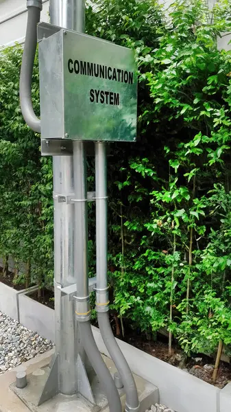 Outdoor control metal box of communication system hub and vertical ducts for cables installed on pole with green tree background, construction business