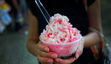 Kadın elleri kırmızı şuruplu plastik bir kaseyi tutuyor üzerine tatlandırılmış konsantre süt sosu konulmuş buzlu sos eğlence marketinde popüler tatlı, seçici bir odak noktası.