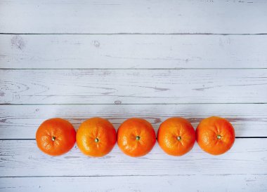 Beyaz ahşap zemin üzerinde 5 taze mandalina, tropikal narenciye meyvelerinin canlı rengi, yaz konsepti, vegan ya da tam besin