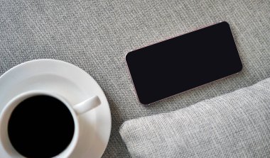 Flat Lay, Top view akıllı telefon modeli ve fotokopi alanı, dijital NOMAD, serbest çalışan işyeri veya online alışveriş konsepti olan kumaş tekstil üzerine bir fincan sade kahve.
