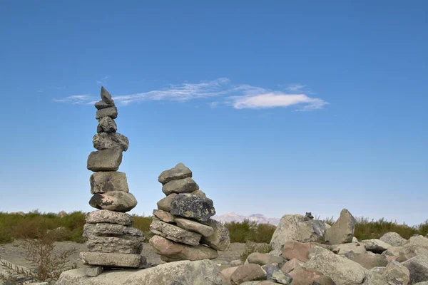 Two stacked rock cairns sitting on a rock with a blue sky background at the Great Salt Lake State Park in Utah.