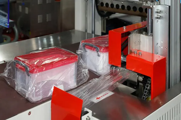 plastic storage boxes are wrapping in transparent plastic film on conveyor belt of packing machine in the plastic container manufacturing.