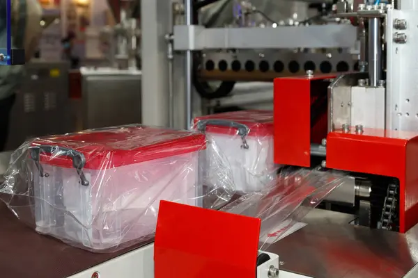 plastic storage boxes are wrapping in transparent plastic film on conveyor belt of packing machine in the plastic container manufacturing.
