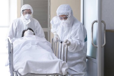 Asyalı hemşire ve doktor takım elbise ve yüz maskesi takarak ciddi şekilde enfekte olmuş koronavirüslü sedye yatağı ya da covid-19 hastası fotokopi alanı olan karantina odasına götürüyorlar. Seçici odak.
