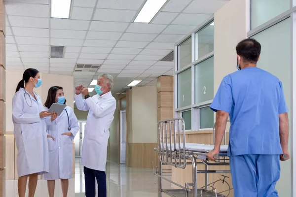 senior professional doctor consult and discuss with woman doctors in serious tumor and cancer surgery case while male nurse pushing stretcher gurney bed in the hospital. medical treatment concept.