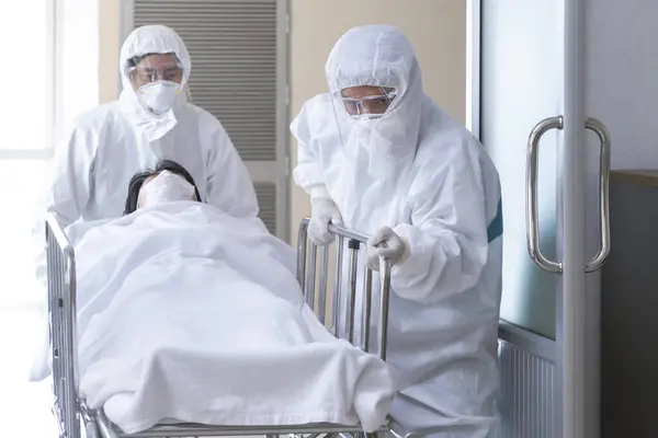 Asyalı hemşire ve doktor takım elbise ve yüz maskesi takarak ciddi şekilde enfekte olmuş koronavirüslü sedye yatağı ya da covid-19 hastası fotokopi alanı olan karantina odasına götürüyorlar. Seçici odak.