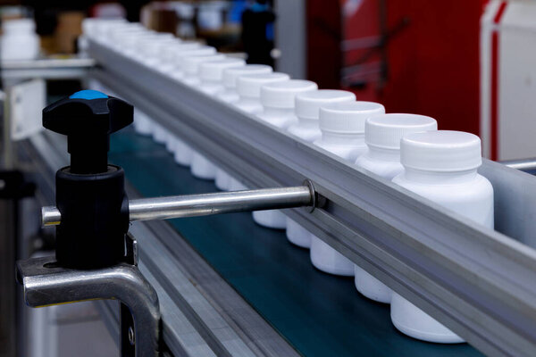 white plastic bottle moving on conveyor belt of auto capping and labeling machine at cosmetic, supplement or medicine pharmaceutical manufacturing.