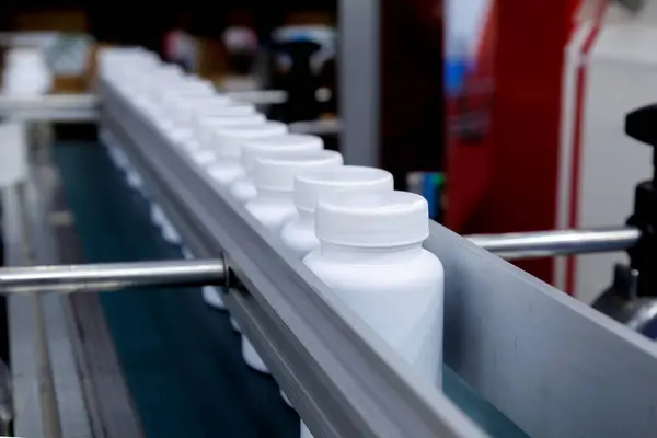 white plastic bottle moving on conveyor belt of auto capping and labeling machine at cosmetic, supplement or medicine pharmaceutical manufacturing.
