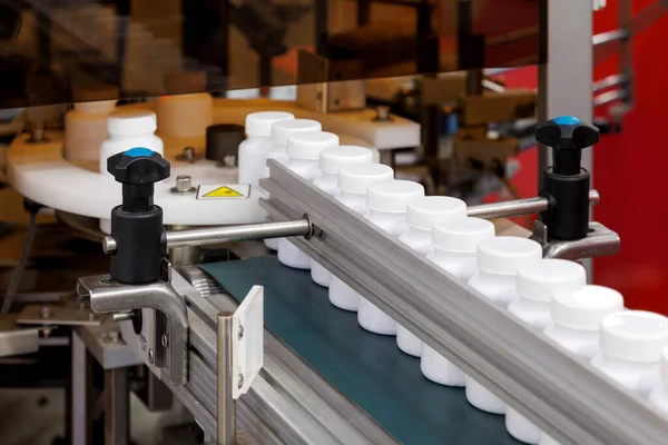 Kozmetik, takviye ya da ilaç imalatında otomatik kaplama ve etiketleme makinesinin taşıma bandı üzerinde hareket eden beyaz plastik şişe.