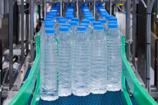 Su şişeleme fabrikasında mavi kapaklı plastik şişeler. Şişelenmiş su üreticisi için endüstriyel üretim hattı.