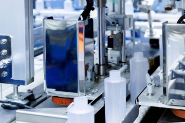 Robot kolu plastik şişeyi kozmetik ve cilt bakımı imalatında otomatik kaplama ve etiketleme makinesinin taşıma bandına taşıyor. Kozmetik endüstrisi ve ai teknoloji makineleri konsepti.